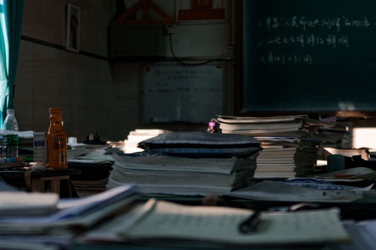 Desks covered with stacks of paperwork and books in a dimly lit room